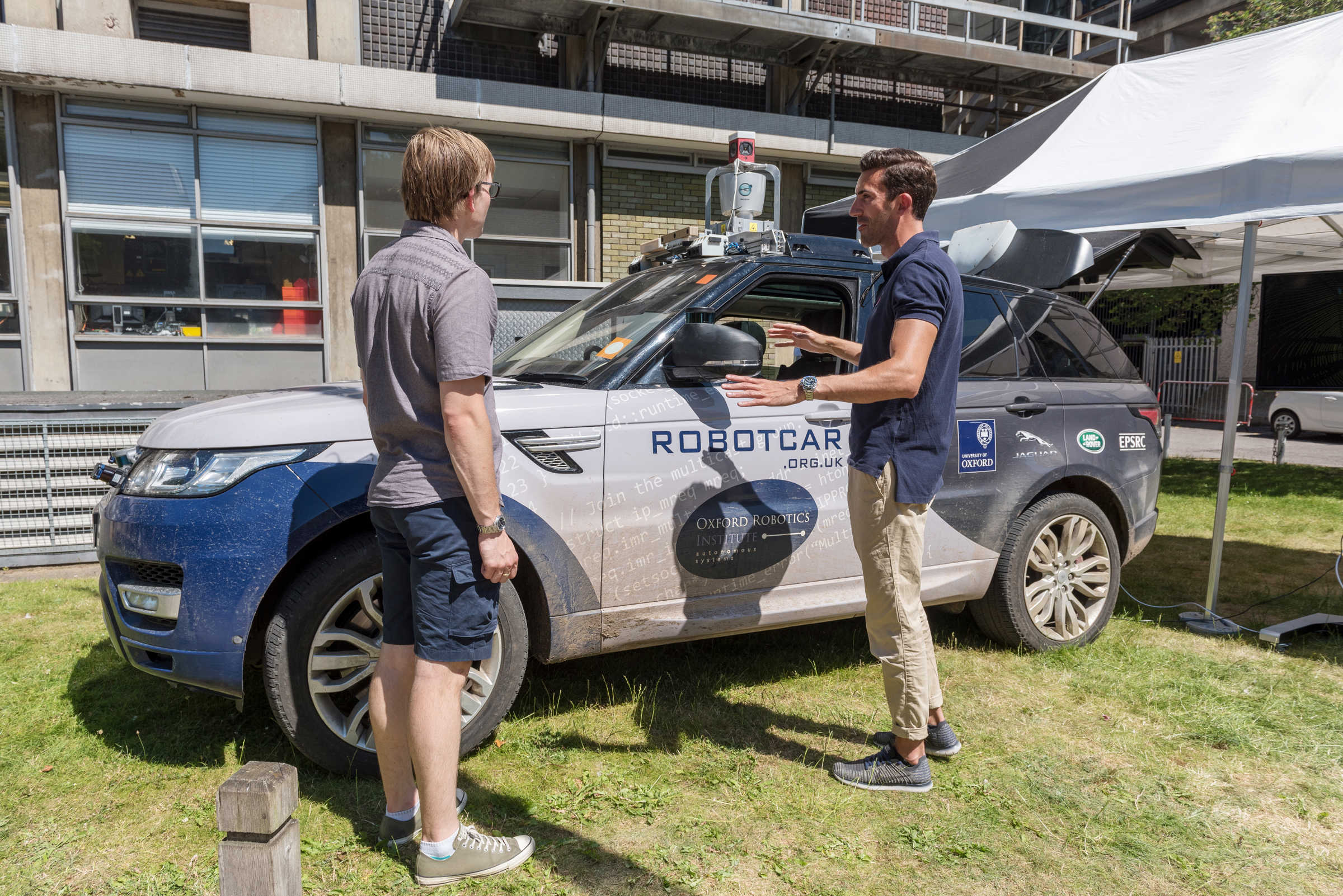 Two people outside talking next to a self-driving car