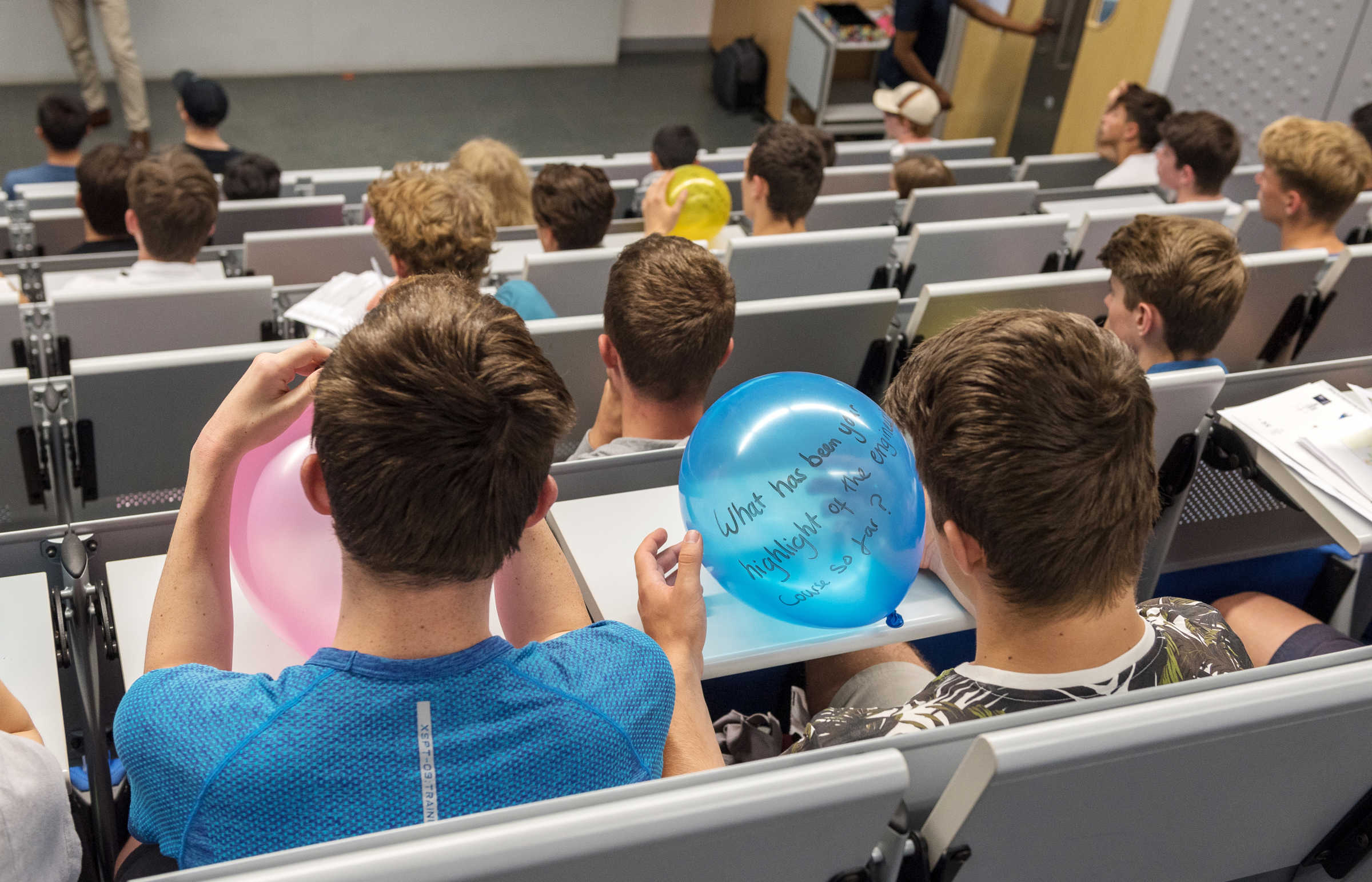 Students in lecture theatre writing questions on balloons